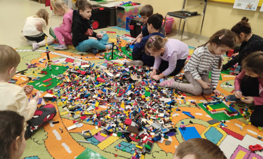 dzieci siedzą na dywanie i budują z  klocków lego
