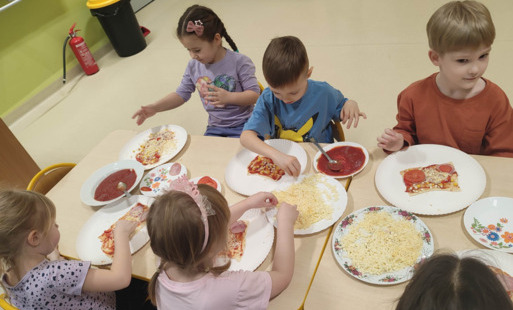 dzieci na przy stole nakładają skałdniki na pizzę
