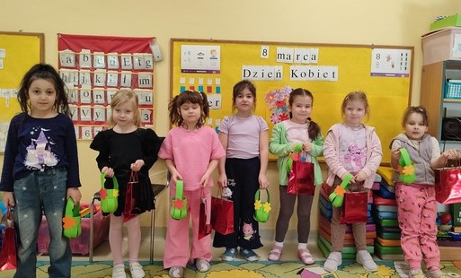 grupa dziewczynek pozuje na tle tablicy z prezentami z okazji dnia kobiet