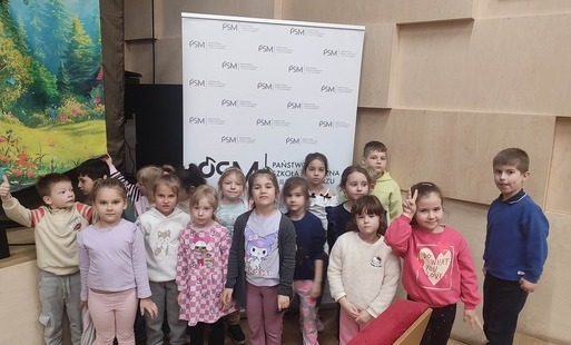 grupa przedszkolna stoi przed sceną w sali muzycznej i pozuje do zdjęcia