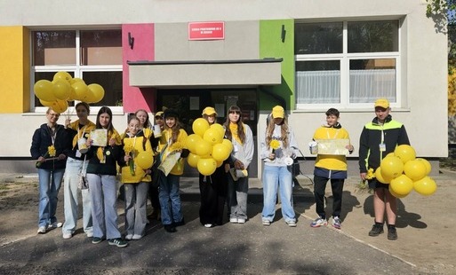 Wolontariusze ze szkolnego koła wolontariatu przed budynkiem szkoły w żółtych koszulkach z żółtymi balonami