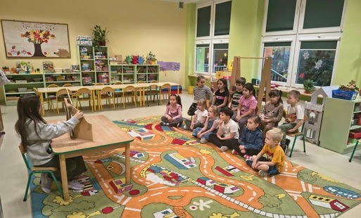 Zdjęcie przedstawia grupę przedszkolną oglądająca opowiadanie pod tytułem „Na tropie śmieciowego potwora w teatrzyku kamishibai.