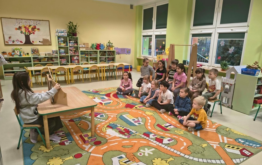Grupa przedszkolna oglądająca opowiadanie pod tytułem „Na tropie śmieciowego potwora” w teatrzyku kamishibai